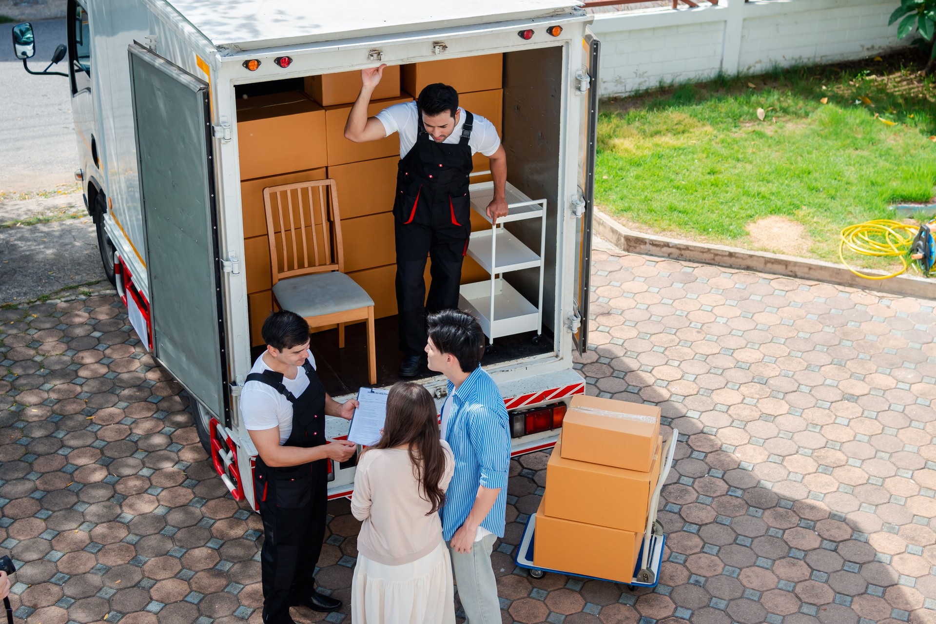 Asian Couple check while unloading boxes and furniture from a pickup truck to a new house with service cargo two men movers worker in uniform lifting boxes. concept of Home moving and delivery.